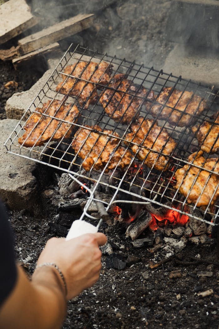 Juicy chicken pieces being grilled over a charcoal fire pit for a delicious BBQ experience.
