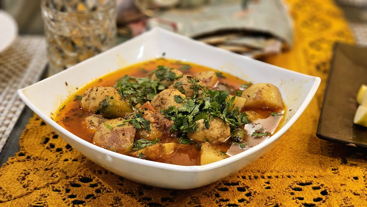Delicious aromatic meatball curry with potatoes and herbs in a white bowl on a table.