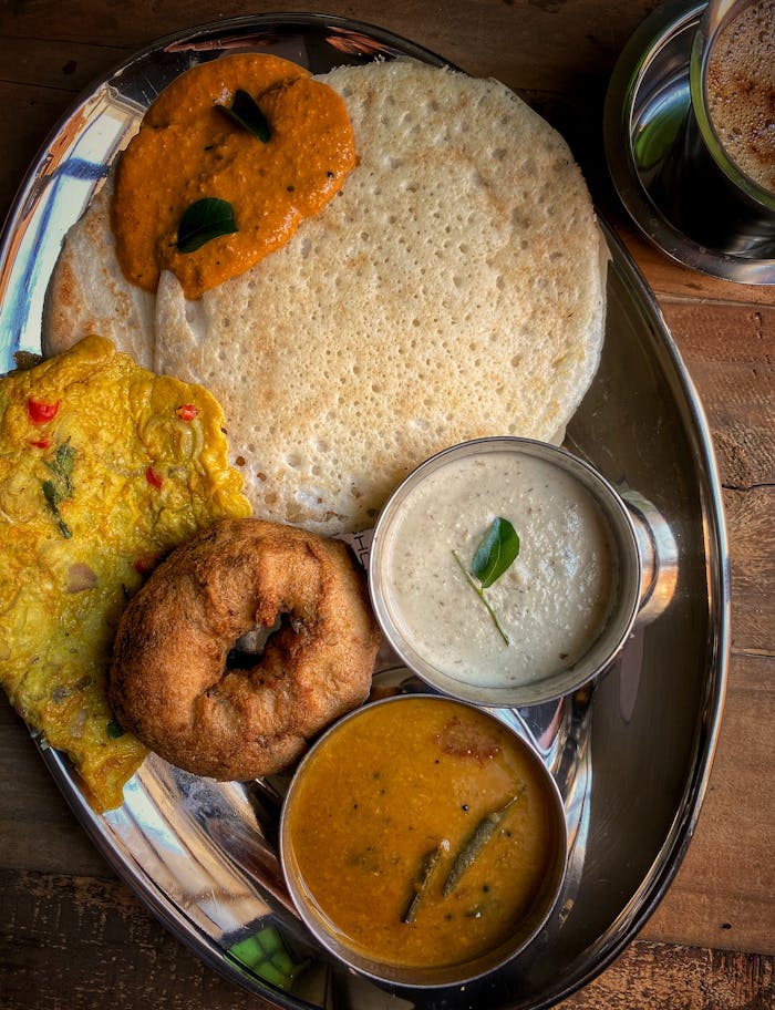 Top view of a traditional South Indian breakfast with dosa, chutneys, and filter coffee.